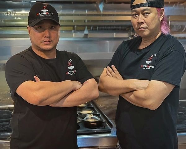 Two chefs posing with arms crossed in a kitchen.