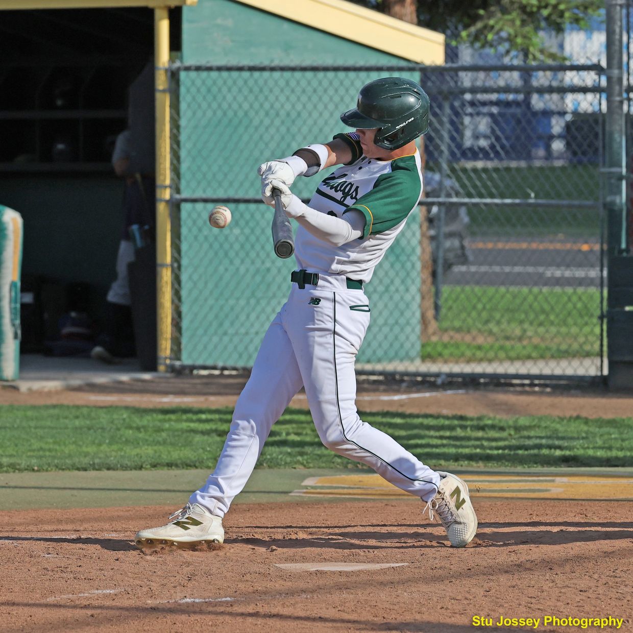 Baseball player mid-swing hitting the ball on a sunny day.