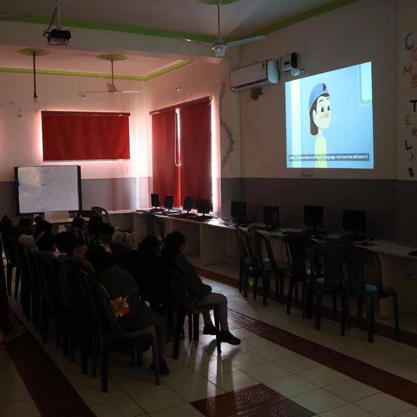 Children watch an animated video in a dimly lit classroom with computers along the walls.