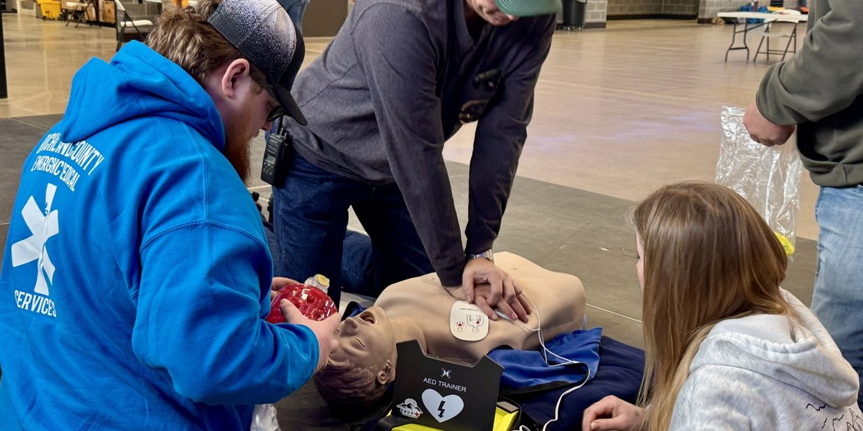 A group practicing CPR and AED use on a manikin indoors.