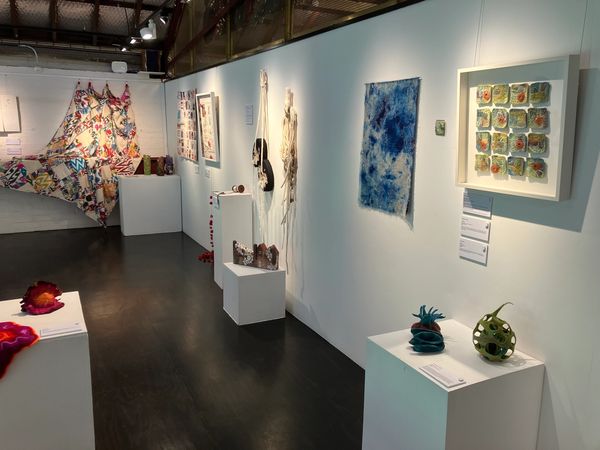 Contemporary art exhibition with diverse textile and sculptural pieces in a well-lit gallery.