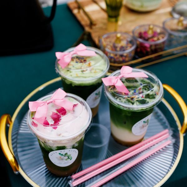 Three decorative iced matcha drinks with pink ribbons on a tray.