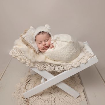 Bebé recién nacido durmiendo con gorro y manta blanca.