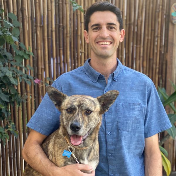A smiling man in a blue shirt holding a happy dog with large ears.