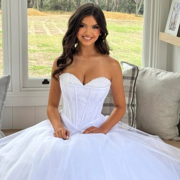 Smiling woman in a white strapless gown indoors.