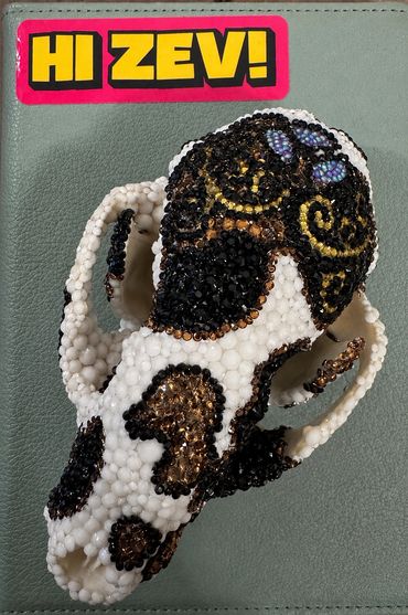 Beaded skull art with intricate black, white, and gold patterns.
