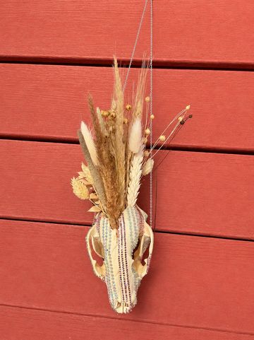 Decorative animal skull adorned with beads and dried plants against a red wooden wall.