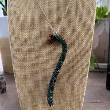Handcrafted necklace with a green beaded pendant shaped like a curved stem.