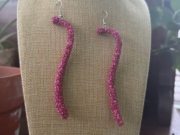 Long, sparkly pink earrings displayed on a bust stand.