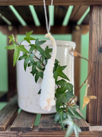 White crystal hanging ornament with green ivy in a ceramic pot on wooden shelf.