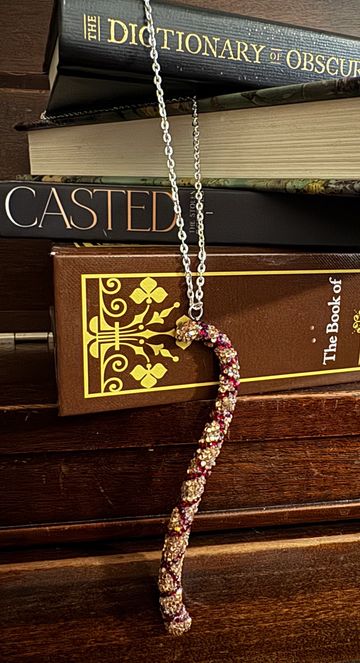 A sparkling candy cane necklace displayed against a stack of books on a wooden surface.