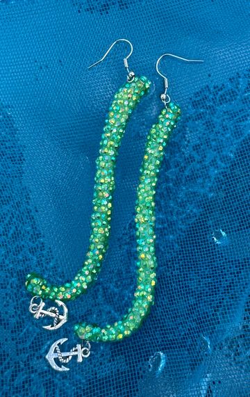 Green beaded earrings with anchor charms on a blue textured background.
