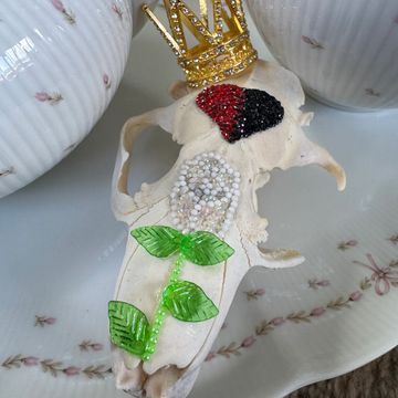 Decorated animal skull with beads and a golden crown on a porcelain surface.