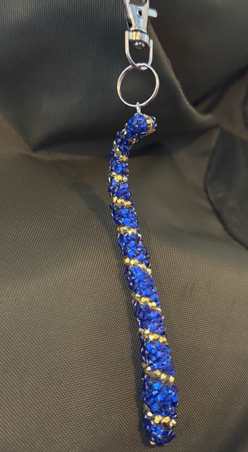 Blue and gold beaded keychain hanging on a black fabric background.