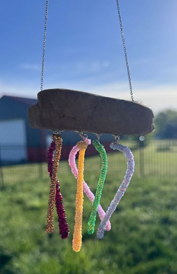 Colorful beaded wind chime hanging outdoors with a blue sky background.