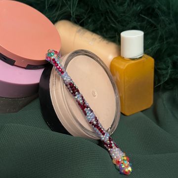 A beaded pen resting on makeup products against a green fabric background.