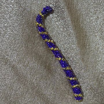 Handcrafted beaded bracelet with purple and gold beads on a textured fabric.