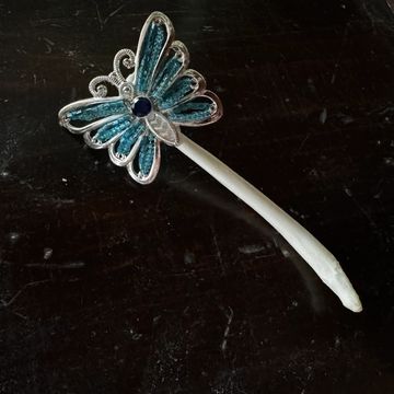 Blue butterfly brooch with white stick on dark surface.