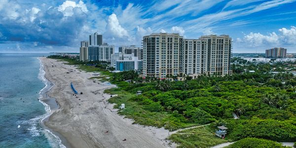A beach with high-rise buildings and lush greenery under a blue sky with clouds.