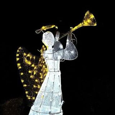 Illuminated angel decoration playing a trumpet at night.