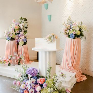 Elegant floral arrangements with pastel colors on draped pink fabric.