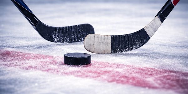 Two hockey sticks near a puck on ice.