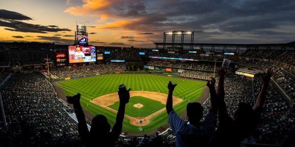 Crowd cheers at baseball stadium during sunset.