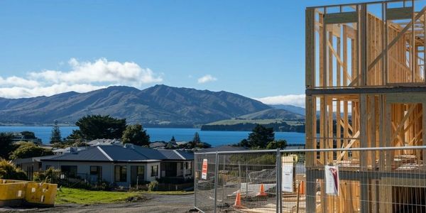 Wooden house frame under construction near a scenic lake and mountains.