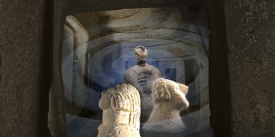 Ancient stone sculptures viewed through layered arches in a dimly lit chamber.