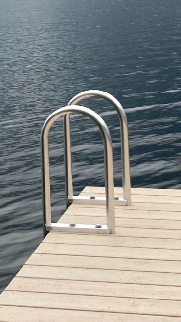 Metal ladder on wooden dock leading into calm water.