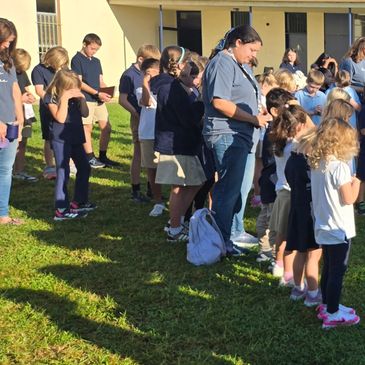 Students and adults standing outdoors in a group on a sunny day.