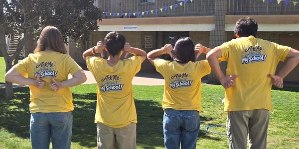 Four students in yellow shirts showing their backs with school-themed messages.