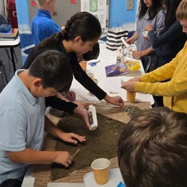 Children and an adult working together on a hands-on project using glue and natural materials.
