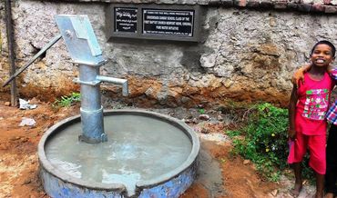 a child standing in front of a hand pump.