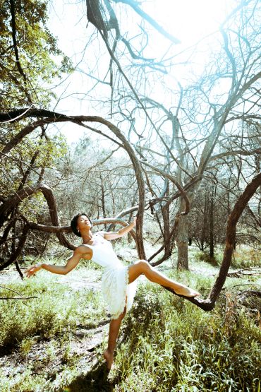 Woman in white dress dances gracefully on a tree branch.