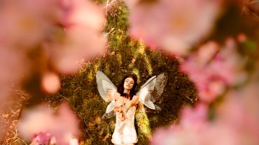 Woman with fairy wings surrounded by pink flowers.