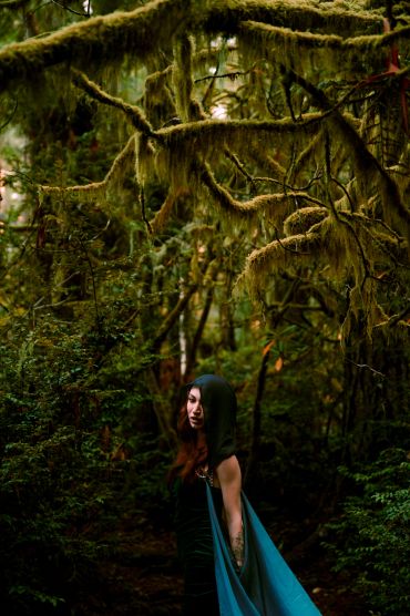 Woman in hooded cloak in mystical forest.