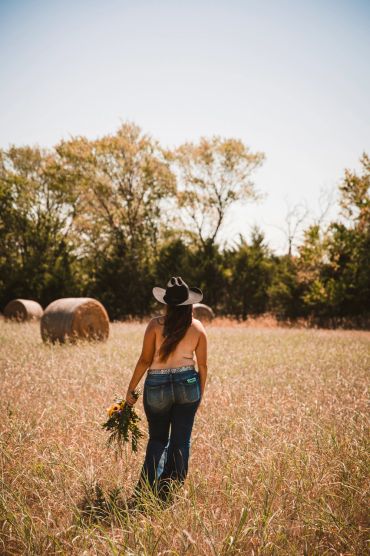Woman with cowboy hat walks through field holding flowers.