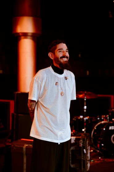 Bearded man smiling on a stage with musical instruments in the background.