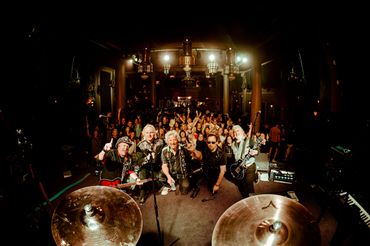 Rock band poses with enthusiastic crowd behind during concert in Tacoma WA