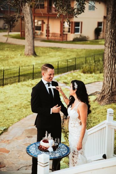 Bride playfully feeding cake to groom outside.