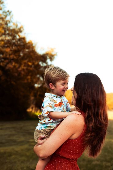 Mother holding and smiling at her young son outdoors.