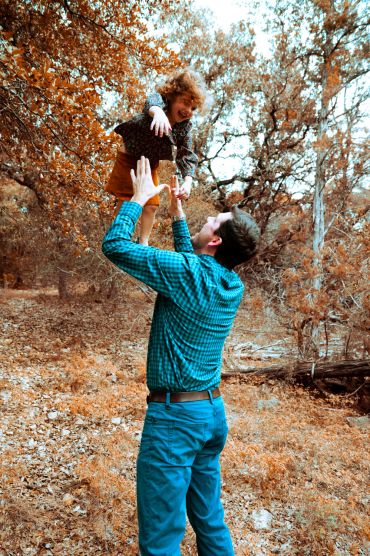 Man joyfully lifts child in autumn forest.