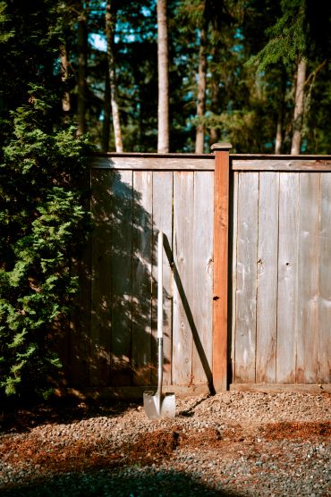 Shovel leaning against a wooden fence in a garden.