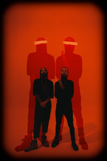 Two men stand with red ghostly shadows and eyes obscured by brush strokes on a vivid red background.