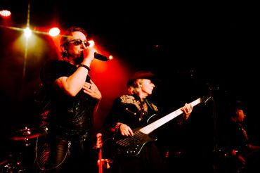 Lead singer passionately performs while bassist plays on stage with vibrant red lighting in Tacoma