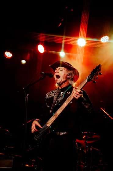 Male musician passionately singing and playing bass guitar on stage under red lights in PNW
