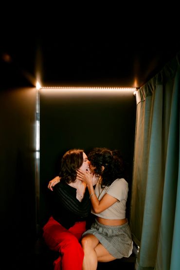 Two women sharing a kiss in a dimly lit space.