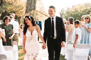 A joyful bride and groom walking hand in hand at their outdoor PNW wedding ceremony.