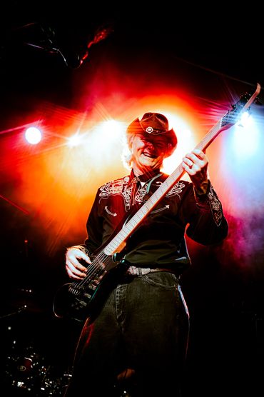 Musician in cowboy hat playing bass guitar on stage with vibrant lighting in Tacoma WA